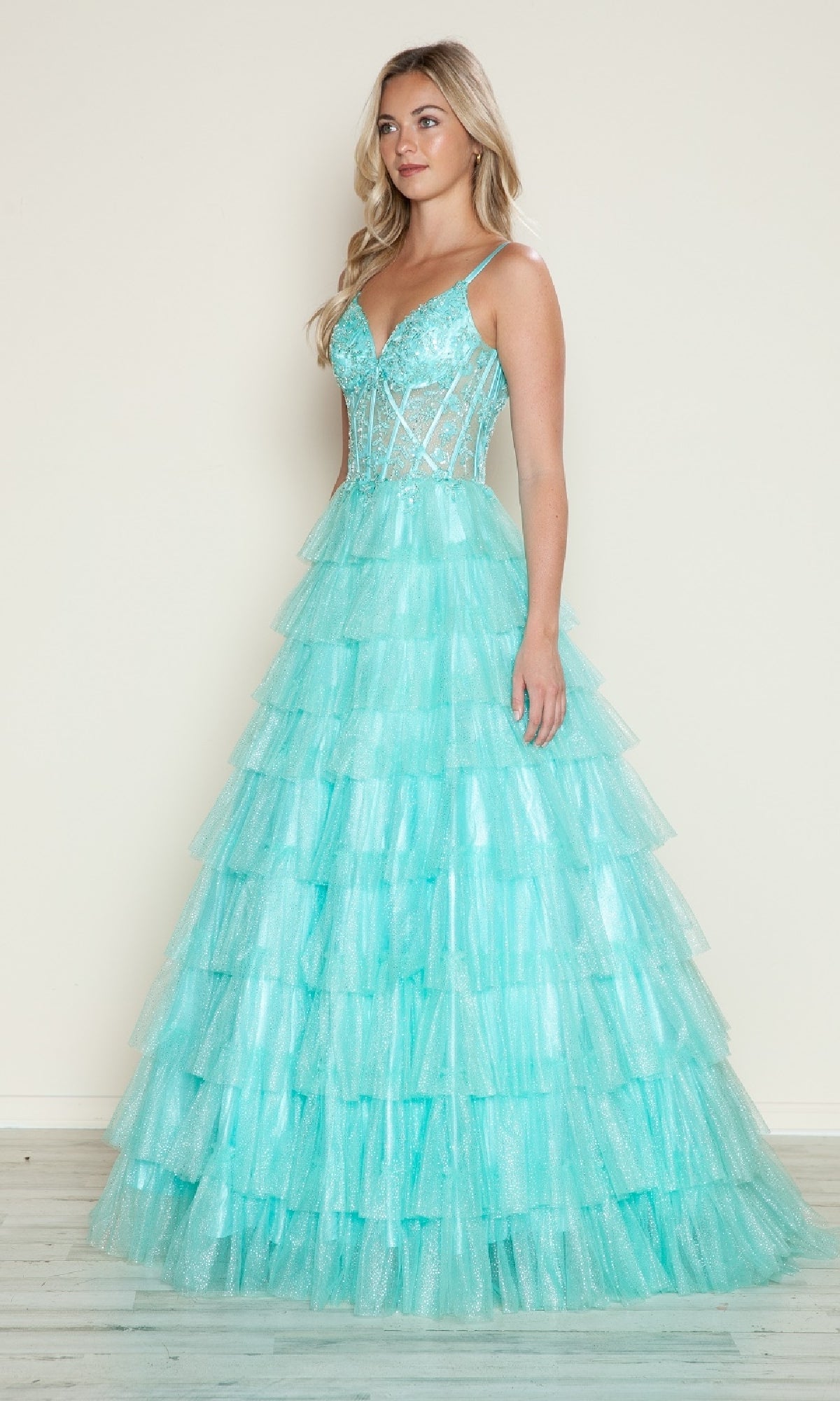 A woman wears the Long Prom Dress: Poly USA 9608—a light blue gown with spaghetti straps, sequined bodice, and tiered ruffled skirt—standing against a plain background.